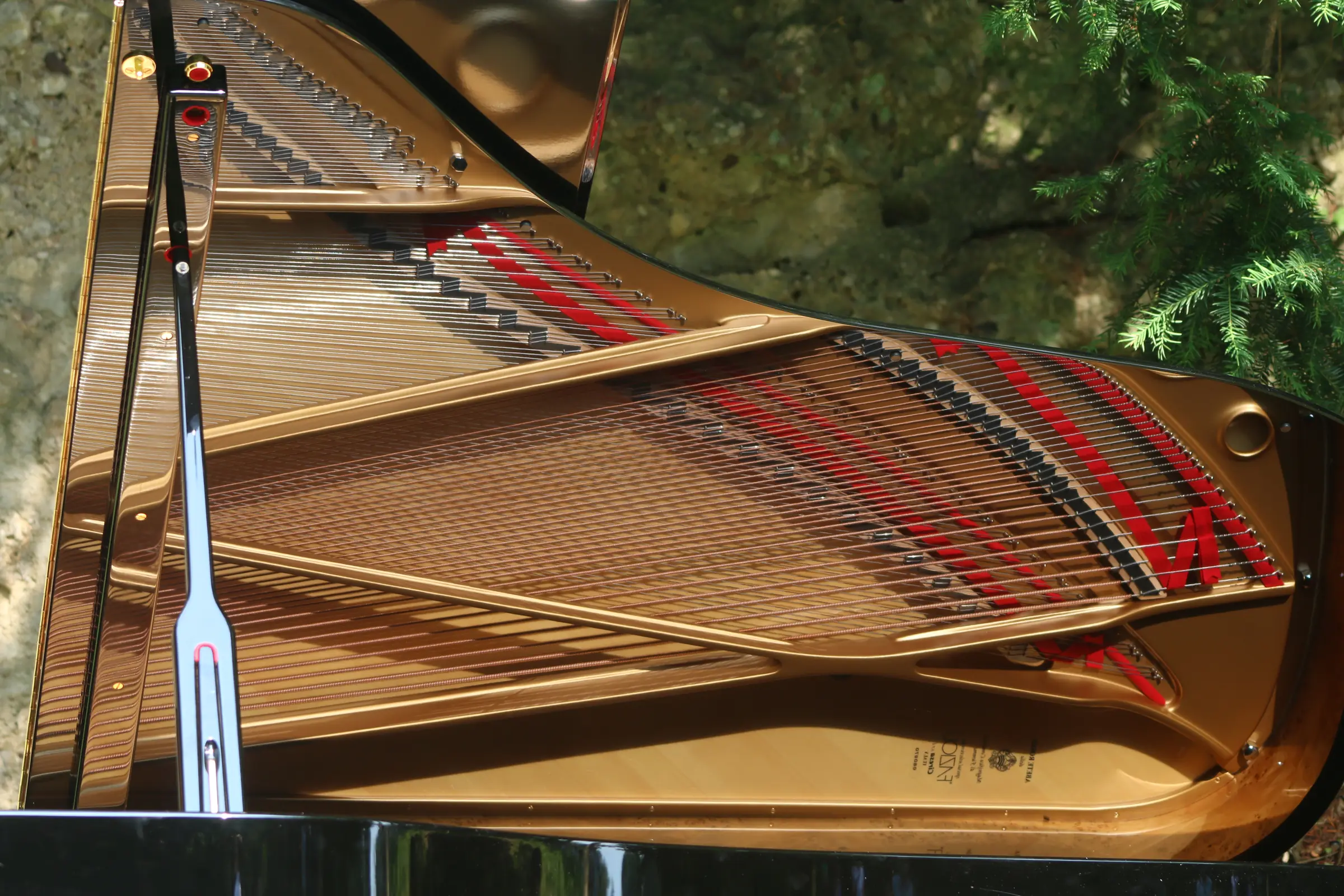 Un pianoforte a coda aperto in un giardino, il telaio dorato e le corde al sole