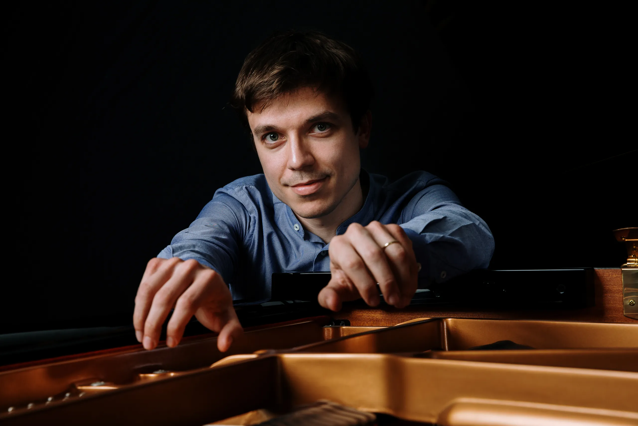 Francesco Di Marco chino sul pianoforte a coda aperto, le mani sul telaio dorato
